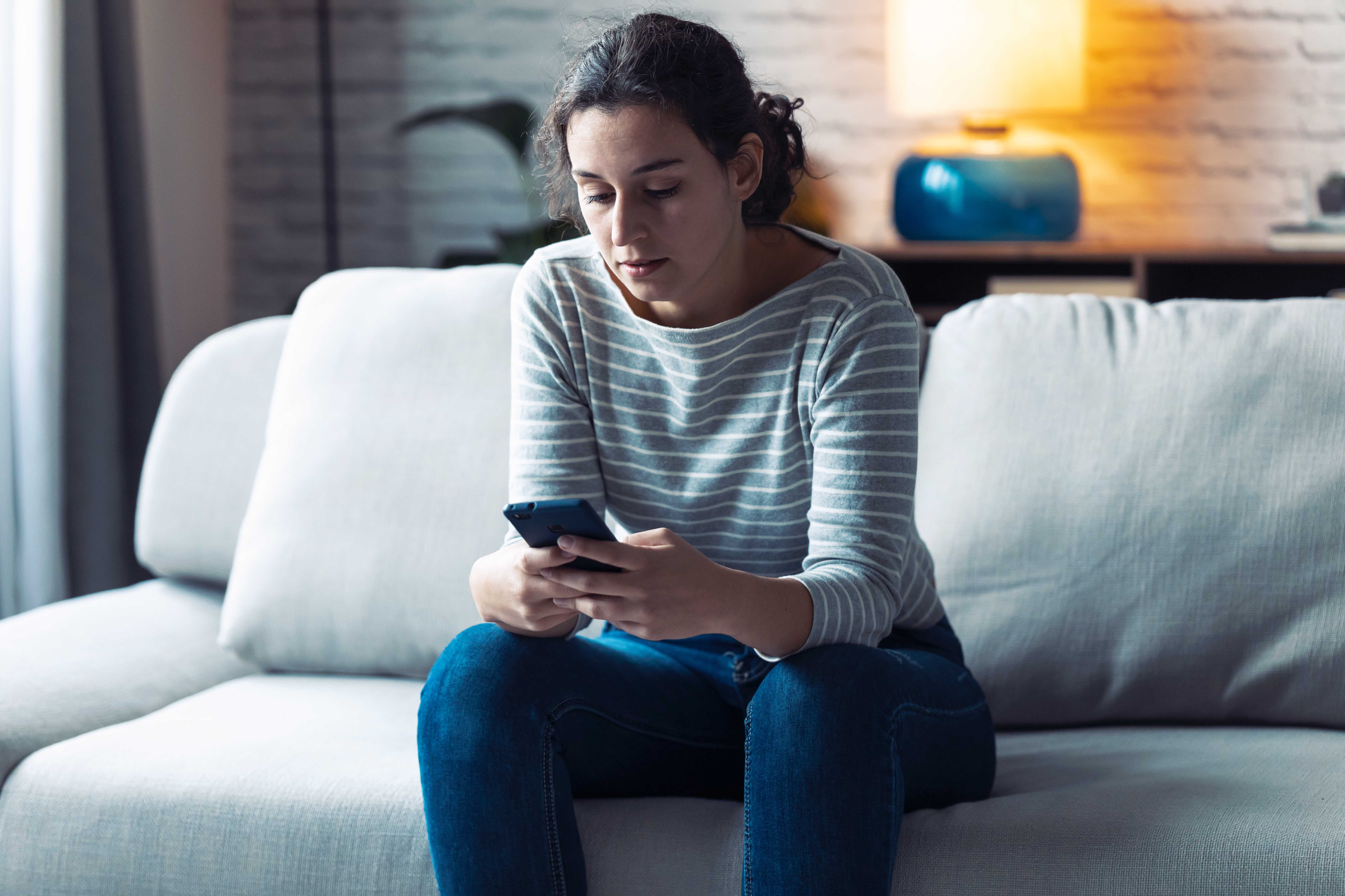 Personne triste assise sur son canapé avec son telephone