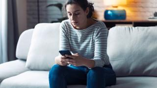 Personne triste assise sur son canapé avec son telephone